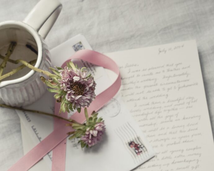 Ein handgeschriebener Brief liegt auf einem Tisch, umgeben von einem frankierten Briefumgschlag, einer Vase und Blumen.