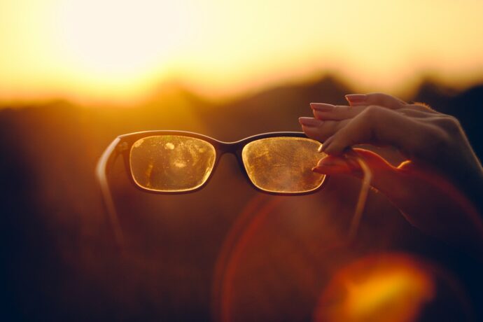 Eine Hand hält eine schutzige Brille gegen den Hintergrund eines Sonnenuntergangs.